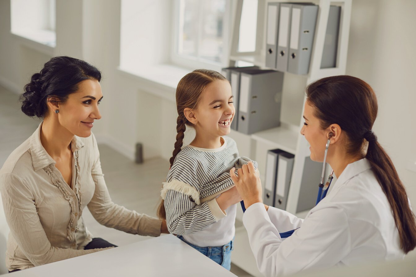 A Woman Pediatrician Makes a Setoscope Examination to a Child Girl with Mom in a Clinic Office.